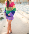 Woman wearing a colorful crochet dress on a beach.