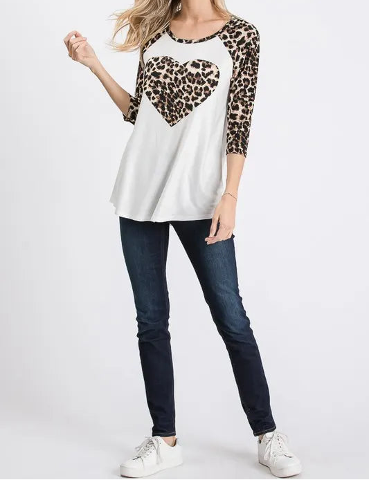 Woman wearing a white top with leopard print heart design and sleeves, paired with dark jeans on a white background.