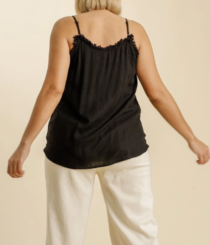 Person wearing a black tank top with thin straps and white pants on a beige background