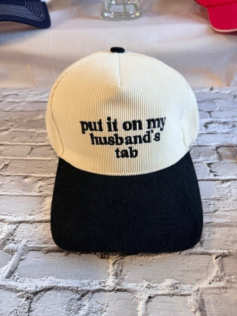 Cap with text 'put it on my husband's tab' on a textured surface