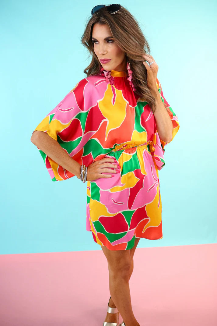 Woman wearing a colorful floral dress against a light blue and pink background