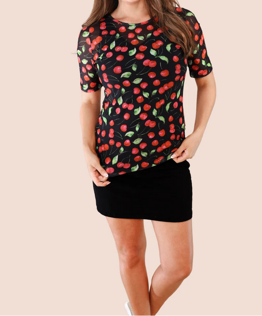 Woman wearing a black skort with a mesh top patterned with red cherries and green stems on a plain background