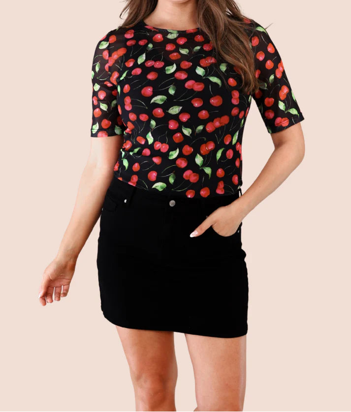 Woman wearing a black skort with a mesh top patterned with red cherries and green stems on a plain background