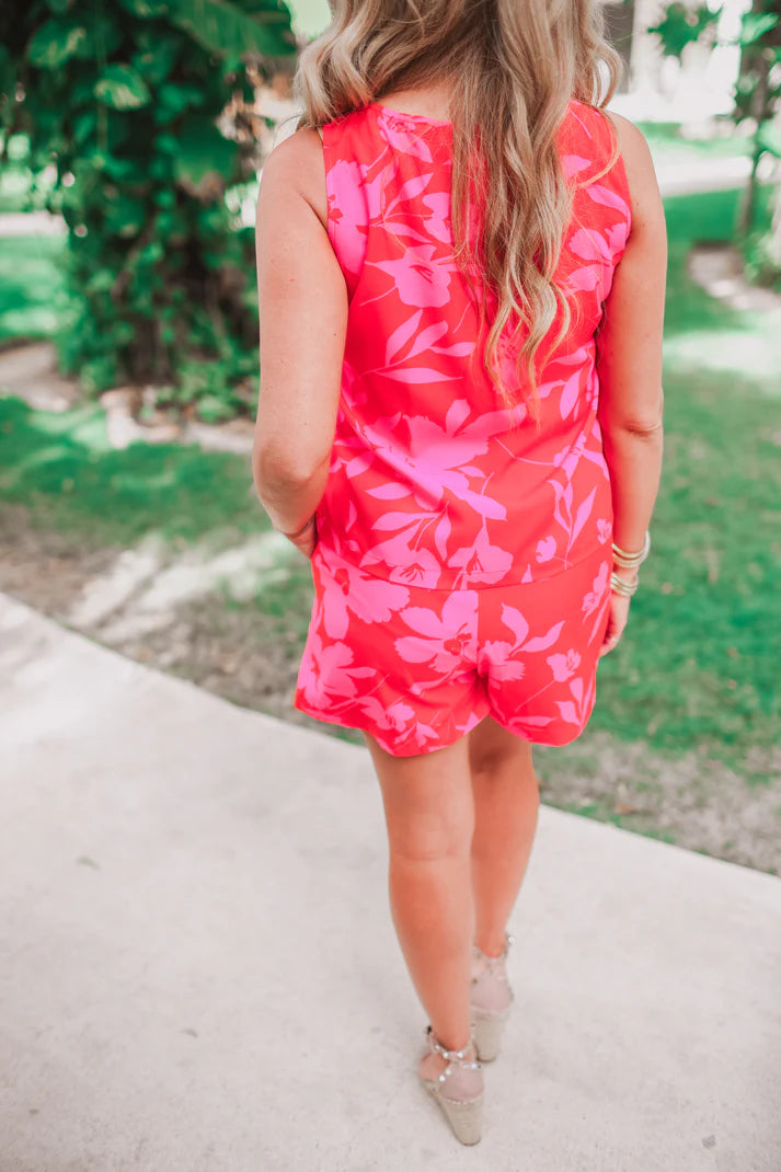 Person wearing a pink floral romper standing outdoors with greenery in the background