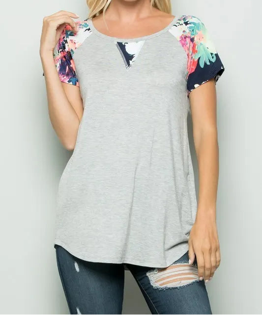 Woman wearing a gray t-shirt with colorful sleeves against a plain background