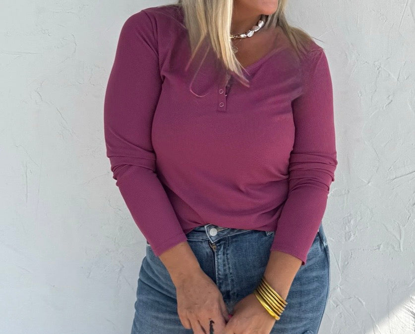 Person wearing a purple long-sleeve top and blue jeans against a white wall