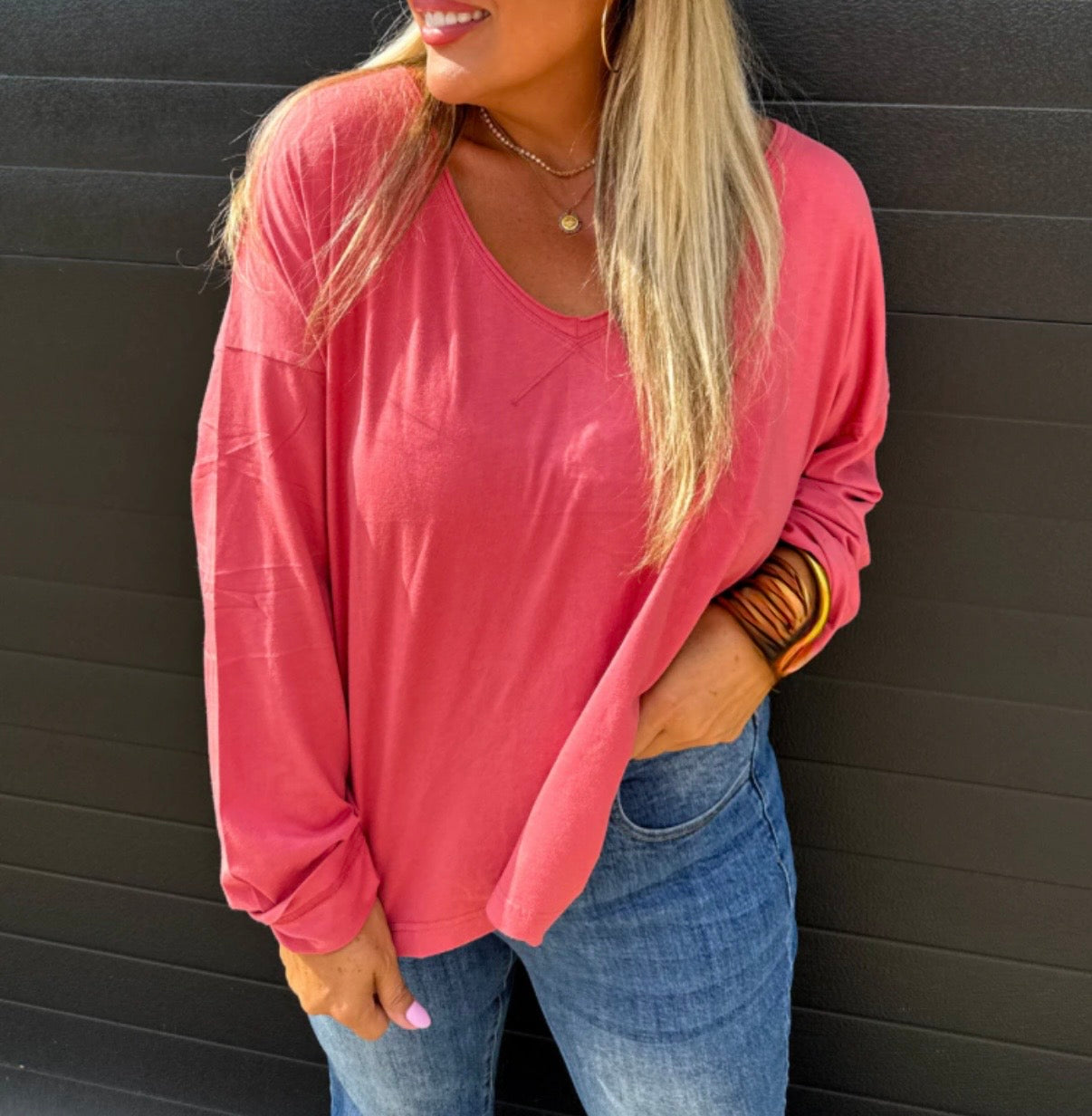 Woman wearing a pink long-sleeve top and blue jeans against a black background