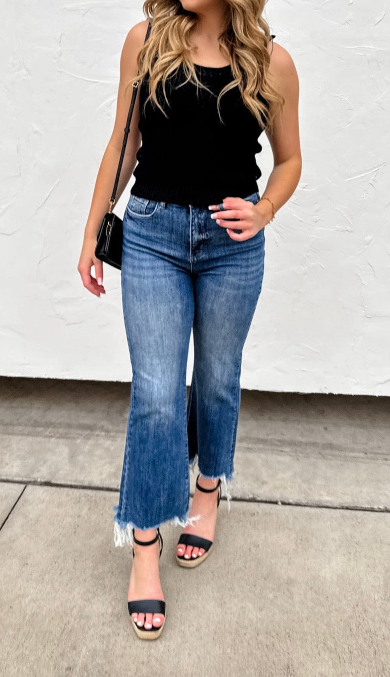Woman wearing a black sleeveless top and blue jeans with a white background