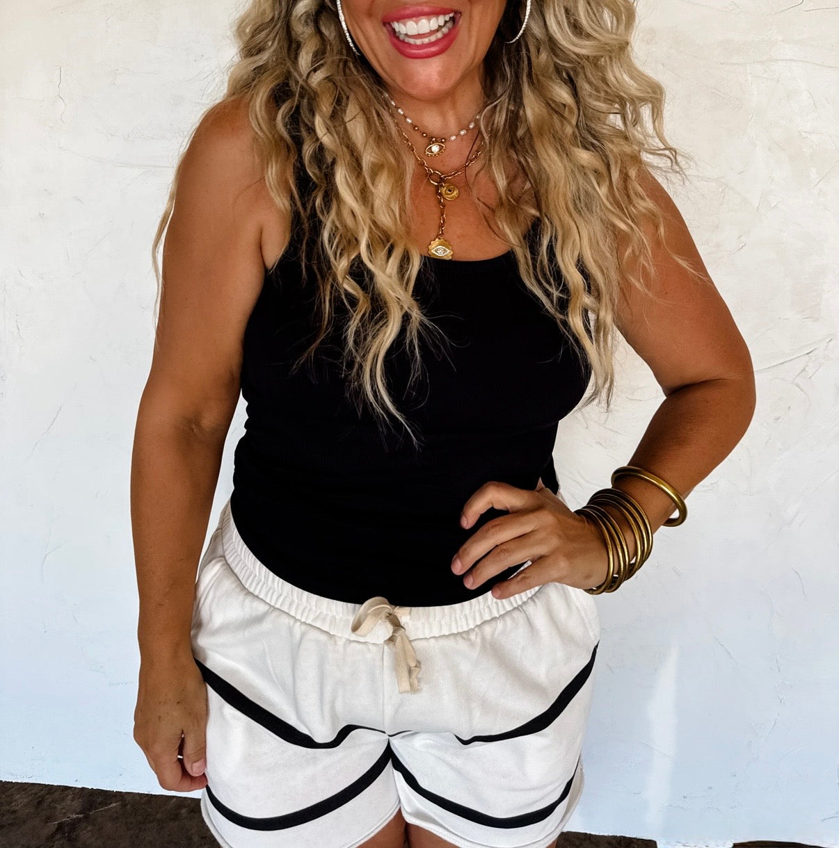 Woman wearing a black tank top and white shorts with black stripes against a white background