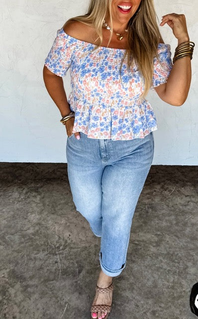 Woman wearing a floral off-shoulder top and blue jeans against a plain background
