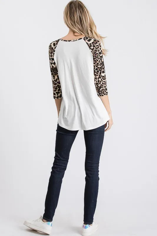 Person wearing a white top with leopard print sleeves and dark jeans on a white background