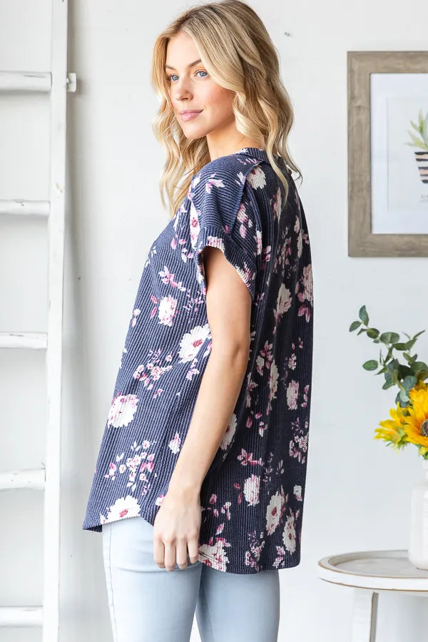 Woman wearing a navy floral blouse in a room with a white wall and a plant.