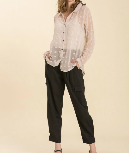 Woman wearing a sheer white blouse with black pants on a beige background