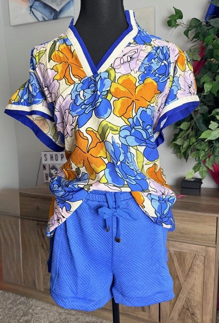Mannequin wearing a colorful floral top and blue shorts in a room setting.