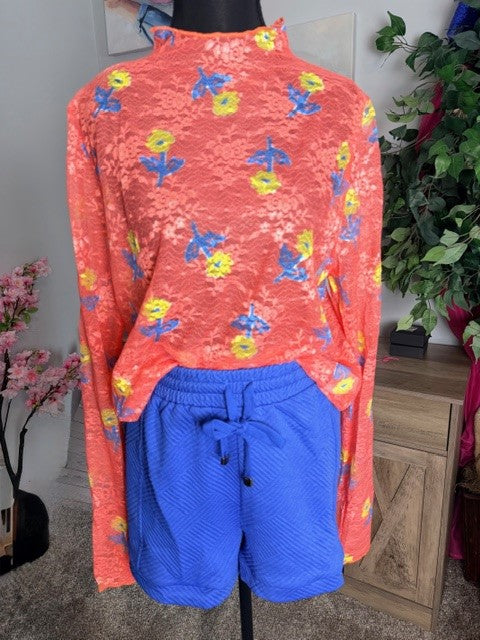 Mannequin wearing a red long-sleeve shirt with colorful patterns and blue shorts indoors.