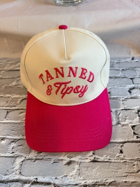 Cap with 'Tanned & Tipsy' text on a brick surface