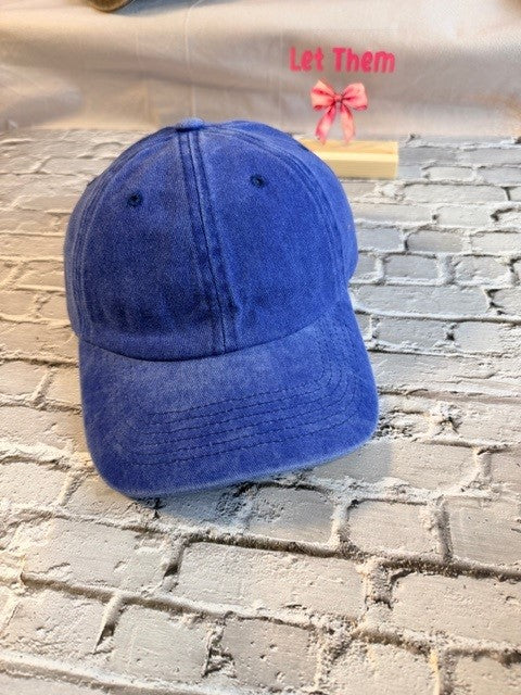 Blue baseball cap on a textured surface with 'Let Them' text and pink bow in the background.