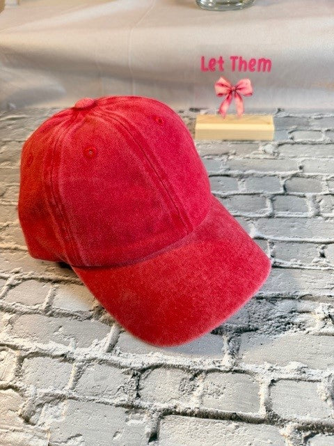 Red cap on a textured surface with text 'Let Them' and a pink bow in the background.