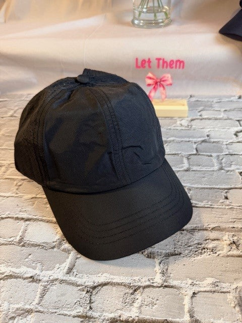 Black cap on a textured surface with 'Let Them' text in the background