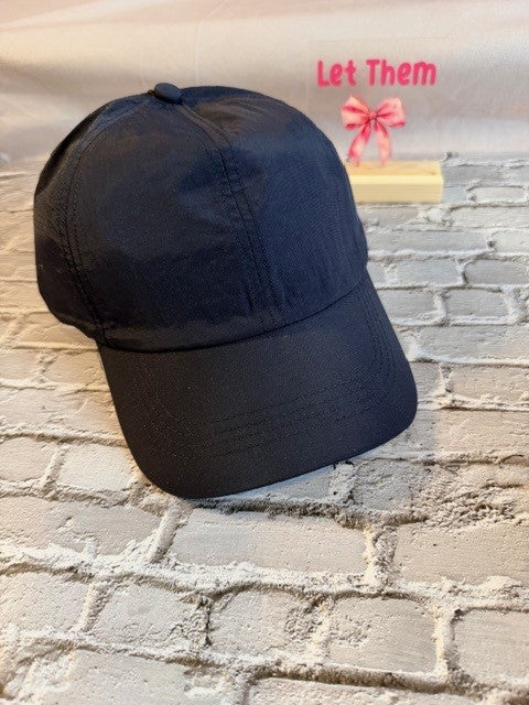 Black cap on a textured stone surface with 'Let Them' text and pink bow in the corner.