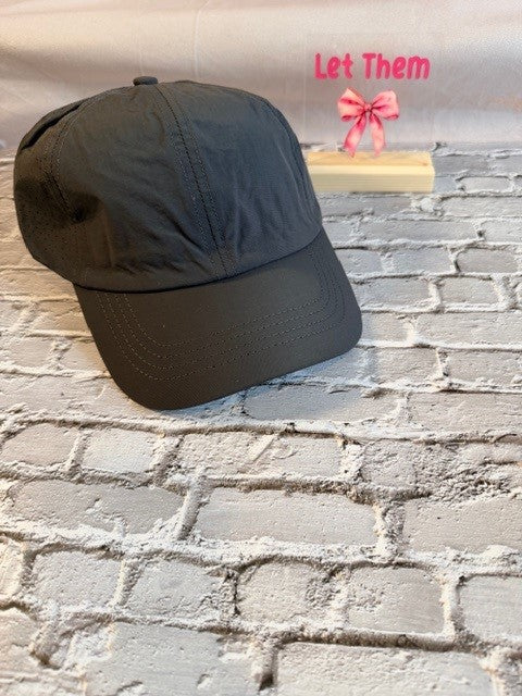 Black cap on a textured surface with 'Let Them' text and pink bow in the background.