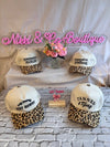 Four leopard print baseball caps with text on a white and gray brick background with 'Nikki & Co Boutique' sign.