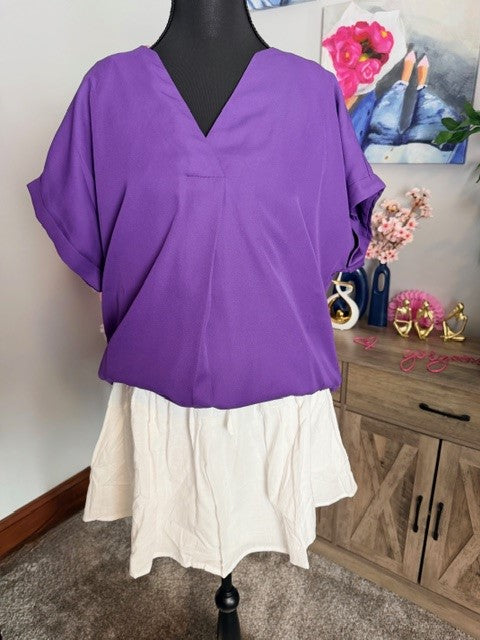 Purple top on a mannequin with a white skirt in a room setting.